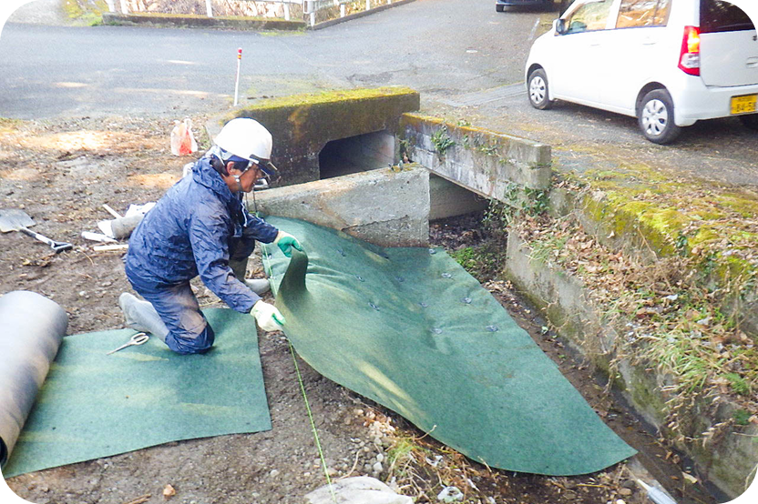 水路付近で防草シートを施工する作業員